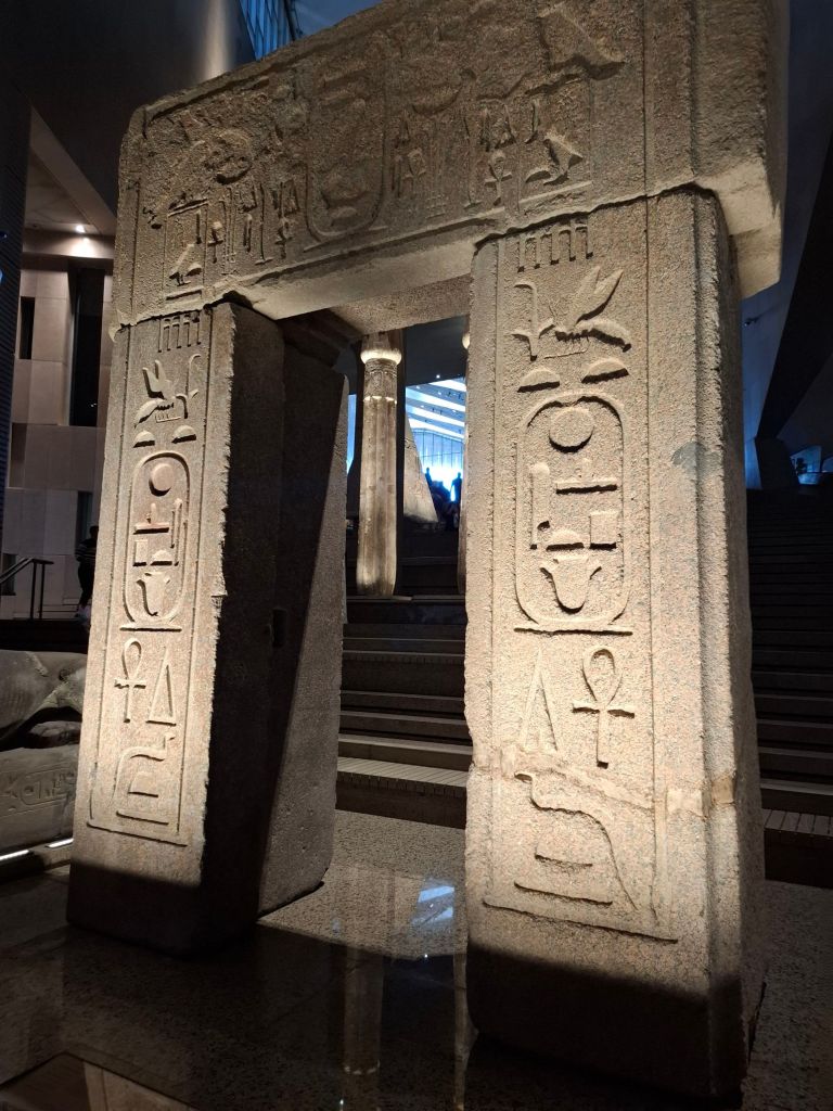 A large granite stone with ancient Egyptian hieroglyphs, displayed in a modern museum setting.