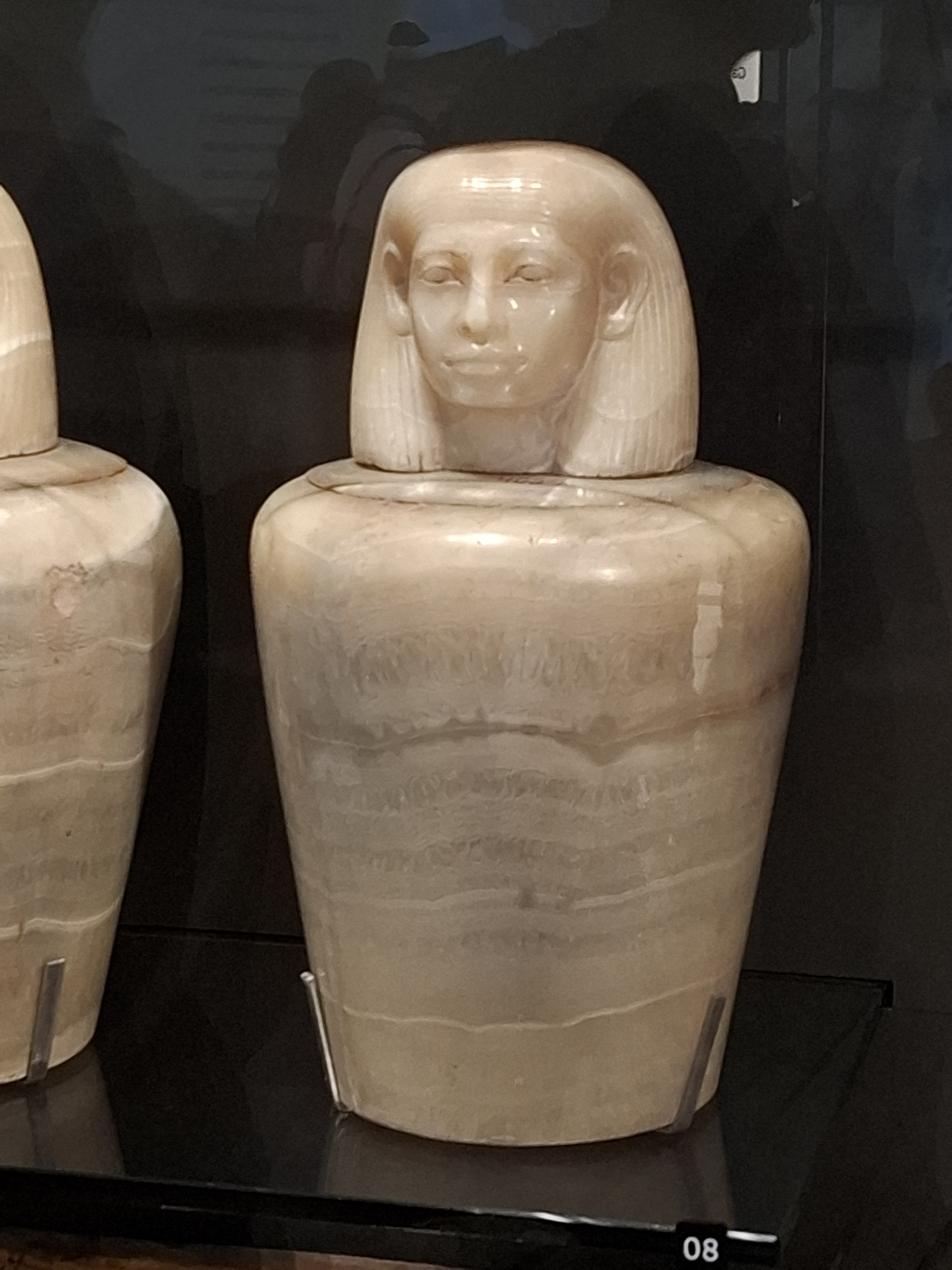 A display of ancient Egyptian canopic jars featuring a detailed carved head resembling a person, made from alabaster.