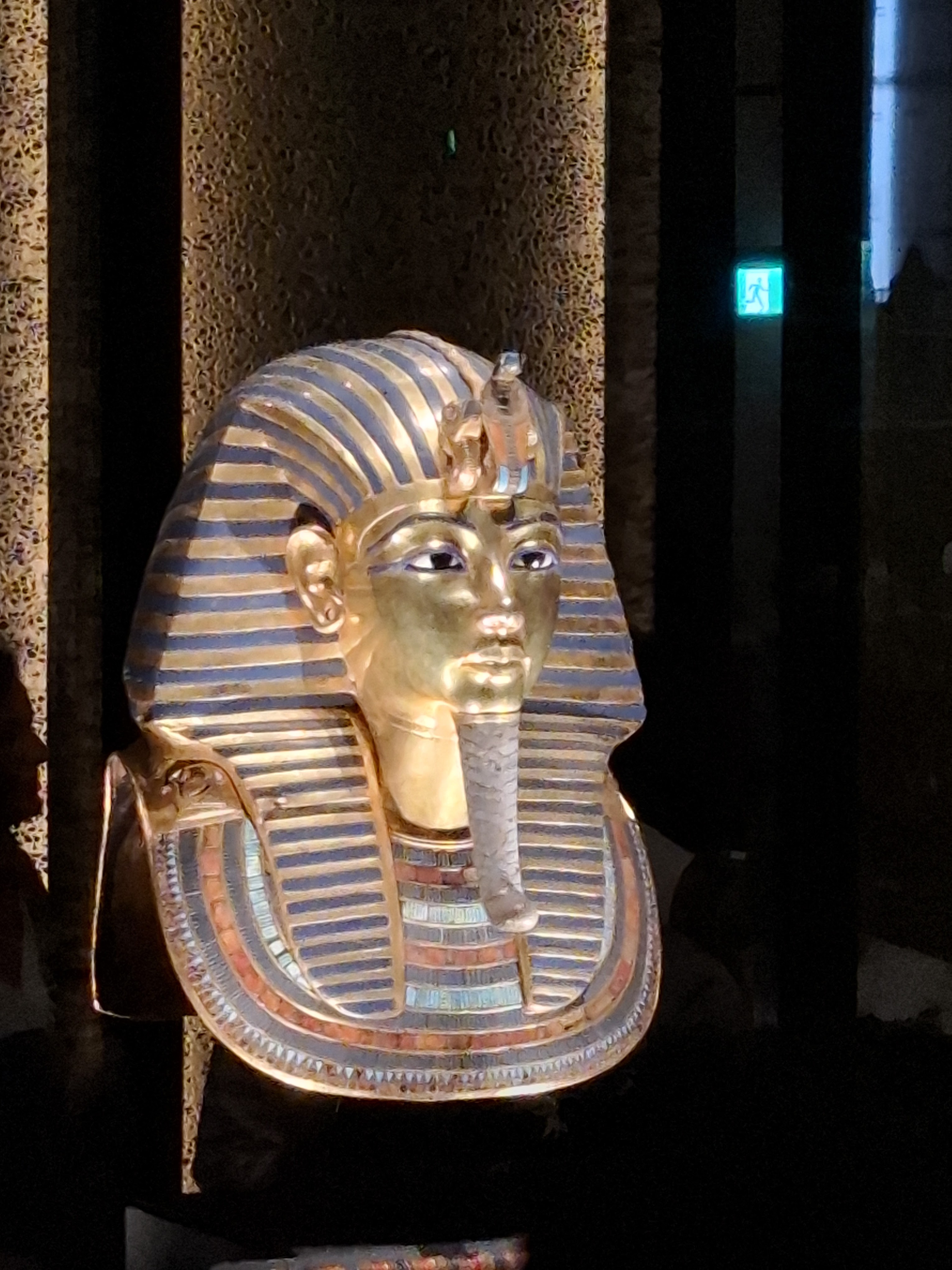 A detailed close-up of the golden funerary mask of Tutankhamun, showcasing intricate patterns and colors, displayed in a museum setting.