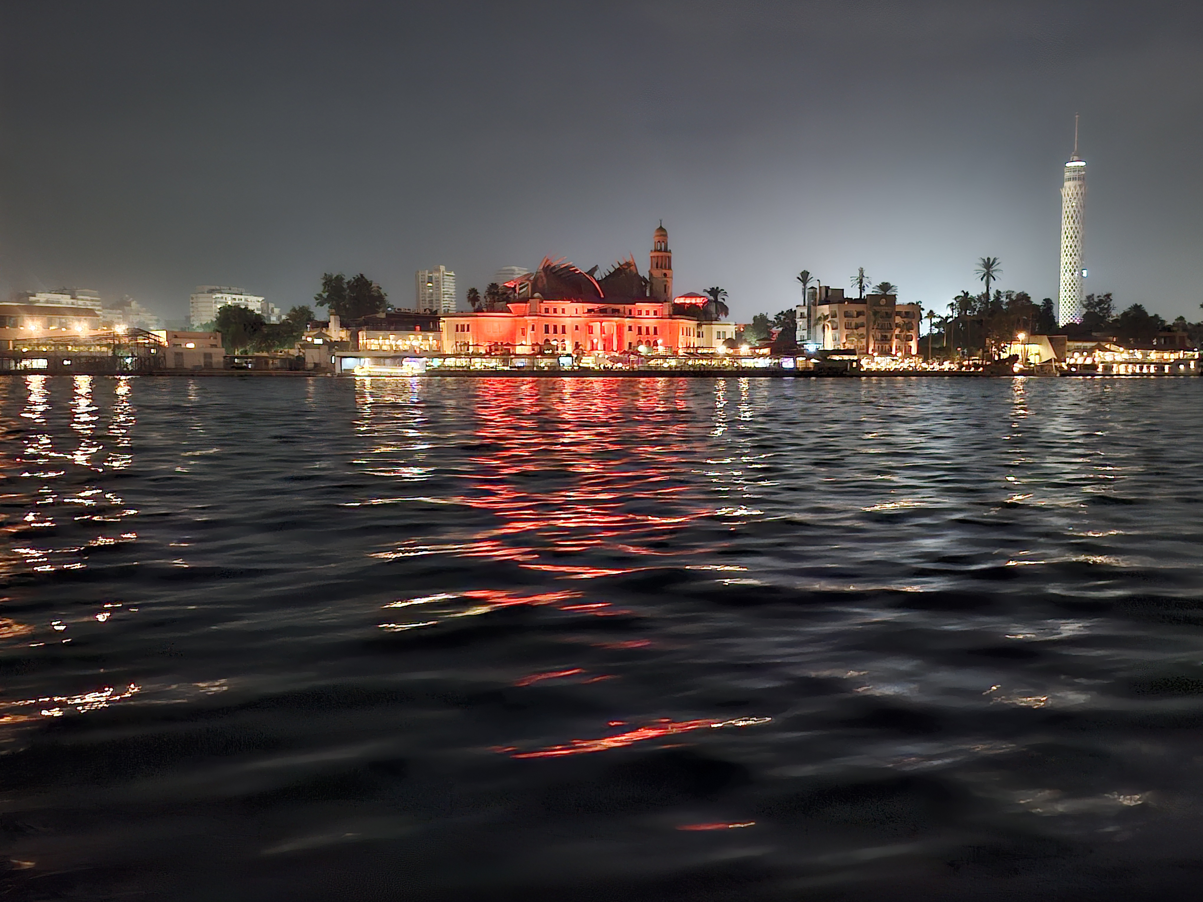 Night view of the Nile River in Cairo, featuring illuminated buildings along the riverside reflecting in the water.