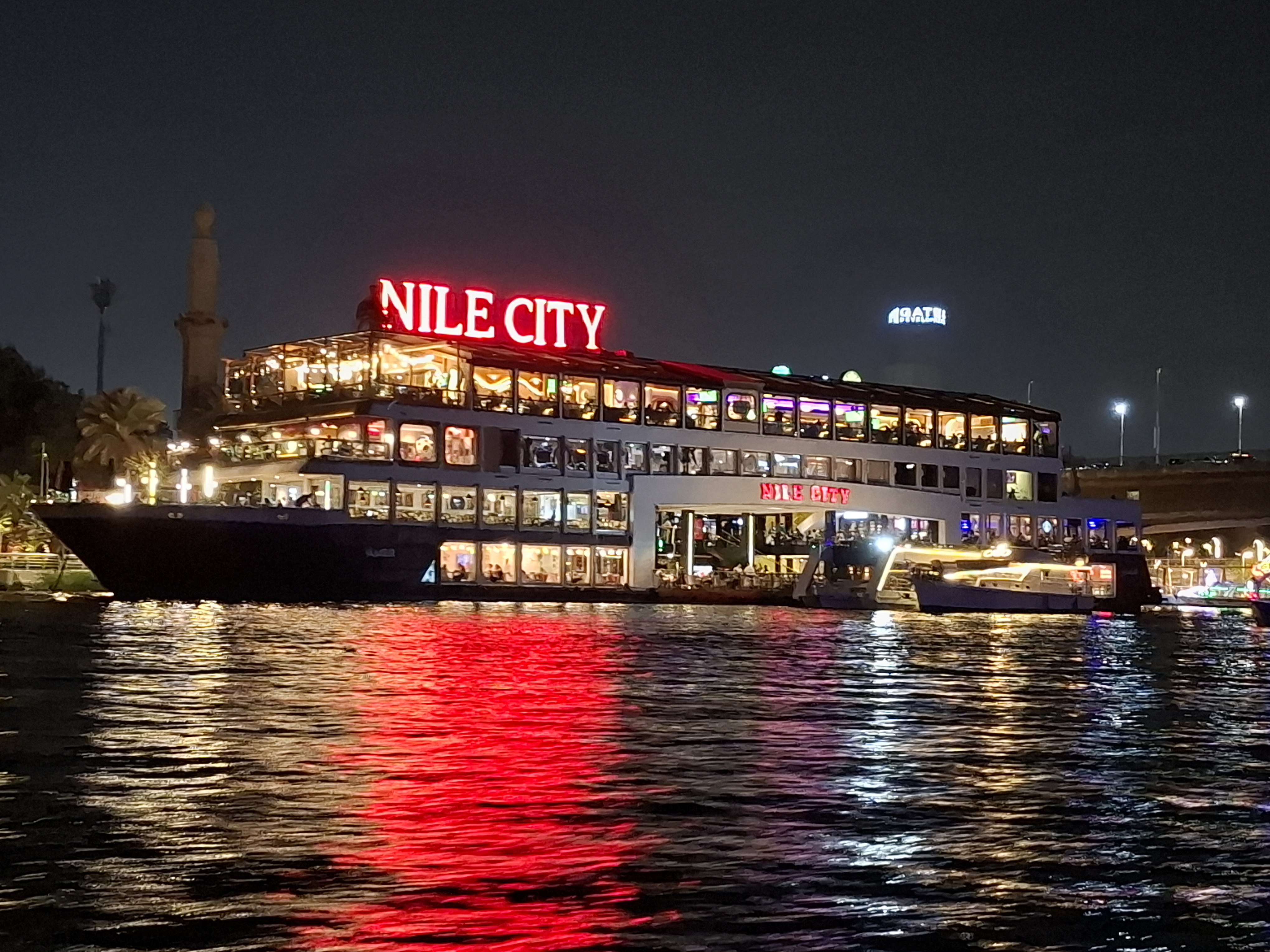 A night view of the Nile City boat restaurant illuminated with bright red lights reflecting on the Nile River, showcasing its vibrant atmosphere.